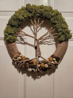 a wreath made out of branches and rocks is hanging on a door with a tree in the middle