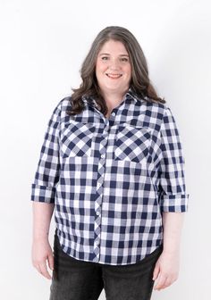 a woman standing in front of a white wall wearing a black and white checkered shirt