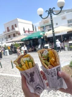 two people holding up some tacos in their hands on the street with buildings in the background