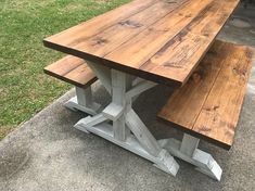 a wooden table and bench sitting on the side of a road in front of some grass