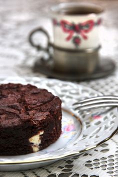 a piece of chocolate cake on a plate with a fork and cup in the background