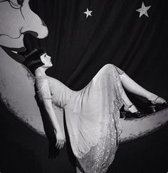 a black and white photo of a woman laying on the moon with stars above her head