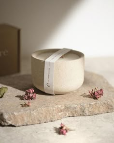 small pink flowers sitting on top of a stone slab next to a box with a white ribbon