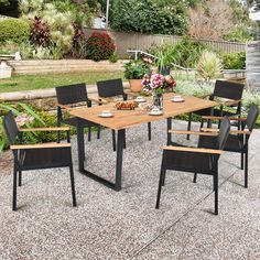 an outdoor dining table and chairs set up in a garden with flowers on the ground