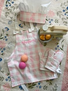 a pink and white checkered table cloth with kitchen accessories on it, including an apron, gloves, utensils, and other items