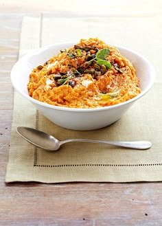 a white bowl filled with food on top of a table next to a silver spoon