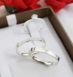 two wedding rings sitting in a box next to a rose