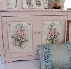 a white cabinet with pink roses painted on the doors and pillows in front of it