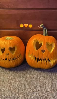 two carved pumpkins with faces and hearts are sitting on the floor next to each other