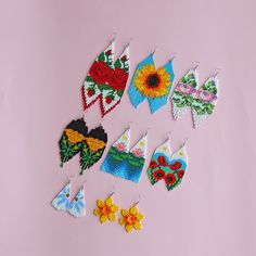 a collection of embroidered earrings with flowers and designs on them sitting on a pink surface