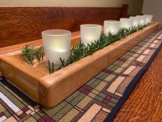 a wooden tray with candles and greenery in it