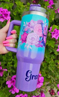 a person holding a purple cup with flowers painted on it and the word grad written in blue