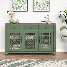 a green sideboard with glass doors in front of two paintings