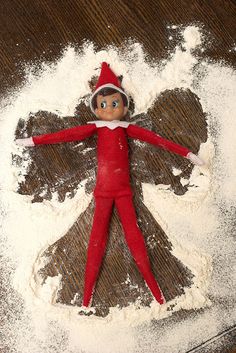 an elf doll laying on top of some white powdered sugar next to a pile of flour