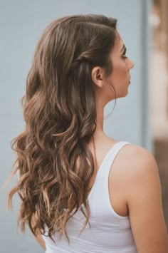 a woman with long hair wearing a white tank top and looking off to the side