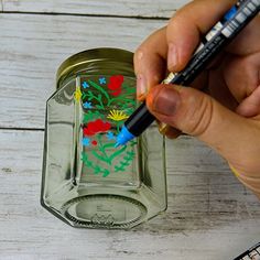 a person is holding a marker and drawing on a glass jar with flowers in it