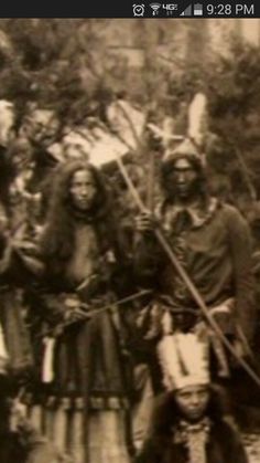 an old black and white photo of people dressed in native american clothing, with spears