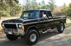 a black pickup truck parked on top of a dirt road next to trees and grass