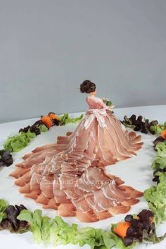 a cake that is shaped like a woman in a dress on top of lettuce and carrots