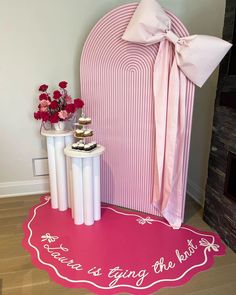 a pink chair with a bow on it next to two white tables and vases