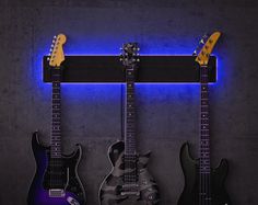 three electric guitars are lined up against a wall with blue light behind them and one is black