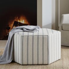 a striped ottoman sits in front of a fireplace with a blanket on it's back