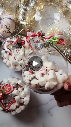 a person holding a glass ornament filled with marshmallows on top of a table