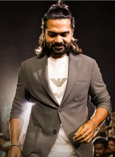 a man with long hair wearing a suit and white t - shirt standing in front of a crowd