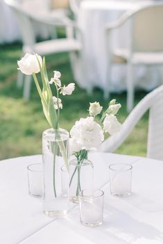 three vases with flowers are sitting on a white tablecloth at an outdoor event