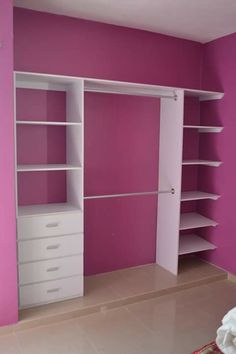 an empty room with pink walls and white shelves on the wall, in front of a bed