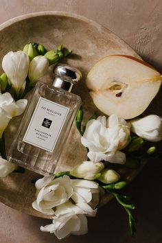 an apple and white flowers on a plate next to a bottle of jo manne