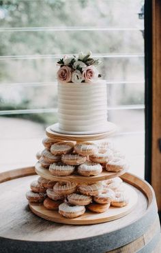 a three tiered white cake sitting on top of a wooden barrel filled with donuts