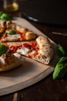 several slices of pizza sitting on top of a cutting board next to some basil leaves