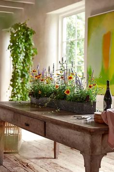 a table with flowers and bottles on it in front of a large painting, next to a window