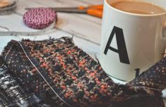 a cup of coffee sitting on top of a table next to a scarf and scissors