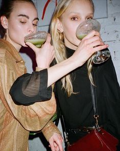 two young women are drinking from wine glasses