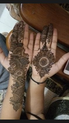 two hands with henna designs on them and a cell phone in the background,