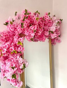 a mirror with pink flowers on it next to a white wall and a gold frame