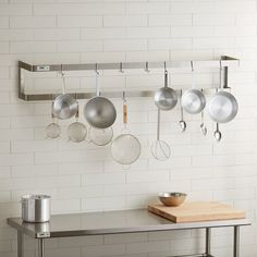 pots and pans are hanging on the wall above a table with a cutting board