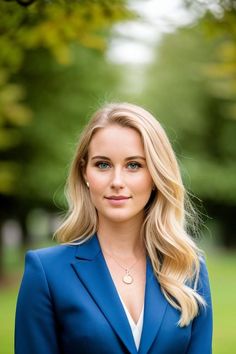 a beautiful blonde woman in a blue suit posing for a photo with trees in the background