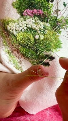 someone is stitching flowers on a pink fabric with needle and thread in their left hand