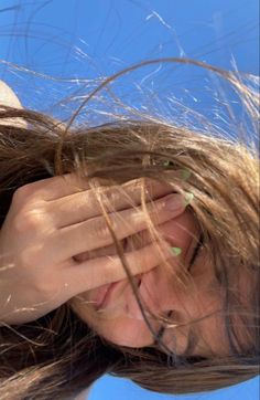 a woman with long hair covering her eyes and holding her hand to her face, against a blue sky