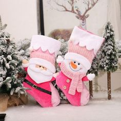 two stuffed santa clauses sitting next to each other in front of snow covered trees