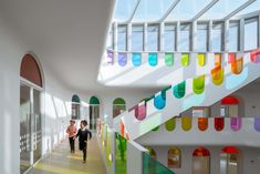 two people walking down a long hallway with multicolored glass windows on the ceiling