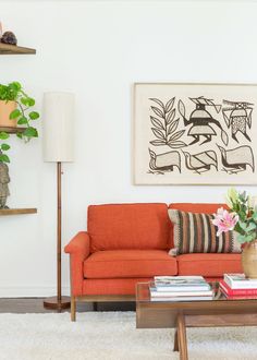 a living room with an orange couch, coffee table and potted plants on the wall