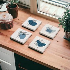 four coasters with blue flowers on them sitting on a table next to a potted plant