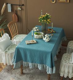 a blue table cloth with white ruffles on it and flowers in a vase