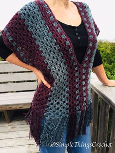 a woman wearing a crocheted shawl standing on a wooden bench with her hands in her pockets