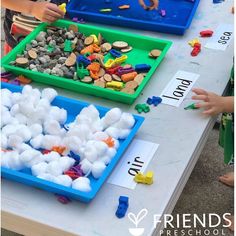 three children are playing with their toys at a table that has plastic trays filled with marshmallows