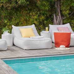 an outdoor lounge chair next to a swimming pool with pillows and drinks on the edge